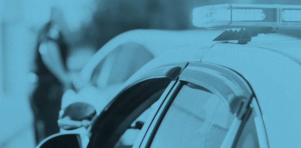 A police car with its light bar visible in the foreground, and an officer conducting a traffic stop in the background, both rendered in a blue-tinted duotone filter.