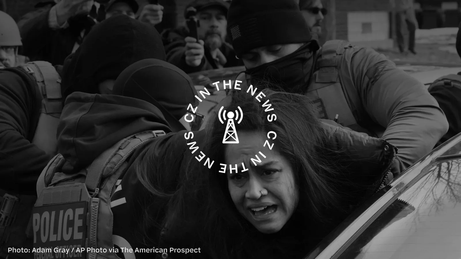 A person is being restrained by police during a protest, surrounded by crowd and photographers.